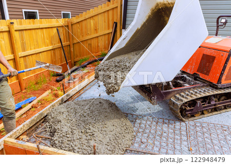 Concrete is being poured from rubber wheelbarrow machine into wooden foundation form for residential construction 122948479