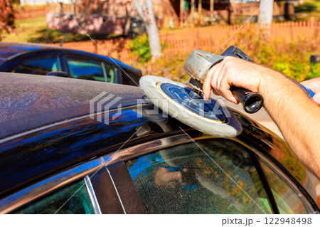 Technician worker is using buffing tool to polish top of dusty car in car service garage Technician worker is using buffing tool to polish top of dusty car in car service garage 122948498