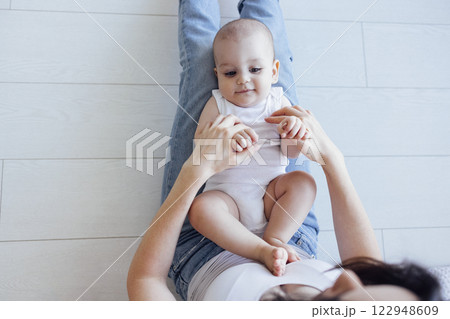 Pretty infant in a white bodysuit with his mom on a light background. 122948609