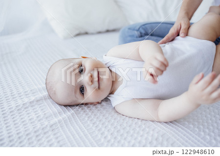 Pretty infant in a white bodysuit with his mom on a light background. 122948610