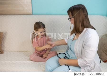 A female pediatrician holds a little girl's hand during a home visit, examining her carefully while building trust and providing the necessary medical support. Concept Medicine and Healthcare. 122948883