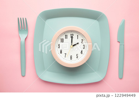 Top view of pink alarm clock with plate, fork and knife on pink background - concept and idea 122949449