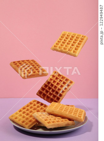 Belgian waffles flying in air on a pasel pink background. Waffles in plate. Creative food concept. Belgian waffles flying in air on a pasel pink background. Waffles in plate. Creative food concept. 122949487