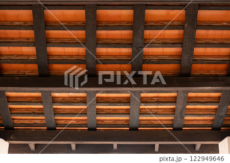 A view from inside a wooden pavilion, with dark wooden beams and terracotta roof tiles 122949646