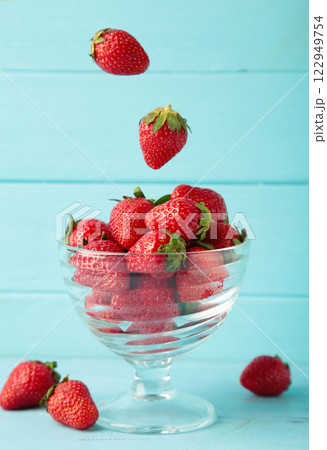 Strawberries fall in glass cup on blue background. Vertical photo Strawberries fall in glass cup on blue background. Vertical photo 122949754