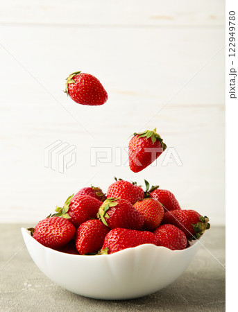Strawberries fall in bowl on light background. Vertical photo 122949780