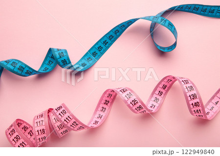 Blue and pink plastic measure tape with metric scale over on color pink background. 122949840