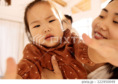 Cute Asian girl in a brown dress with her attractive mom. A smiling Korean woman holds her little daughter. 122950049
