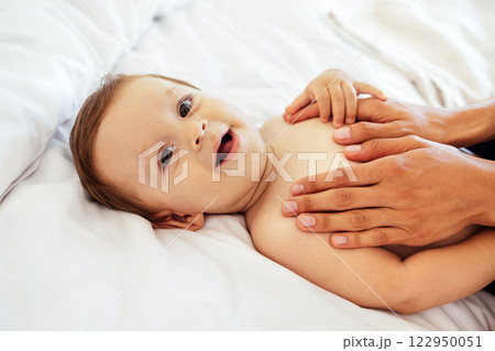 A cute smiling baby and his mom hands. A mother touches her little son tummy. A laughing sweet baby is lying on the bed. A cute smiling baby and his mom hands. A mother touches her little son tummy. A laughing sweet baby is lying on the bed. 122950051
