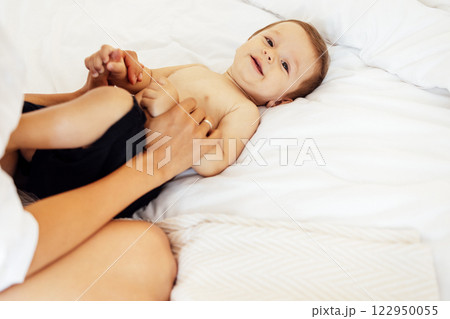 Close-up of a child portrait of a cute little boy lying on a white sheet. Sweet toddler is having fun with his mom in the bedroom at home. Close-up of a child portrait of a cute little boy lying on a white sheet. Sweet toddler is having fun with his mom in the bedroom at home. 122950055