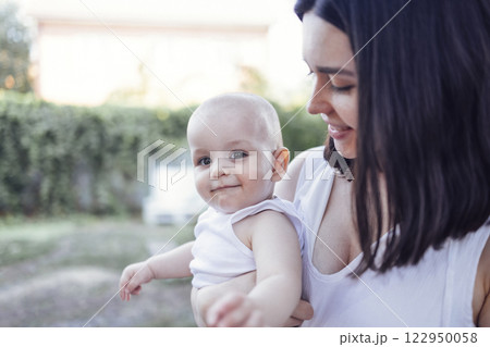 Close up of female portrait of young charming mother holds her cute baby in arms in garden Close up of female portrait of young charming mother holds her cute baby in arms in garden 122950058