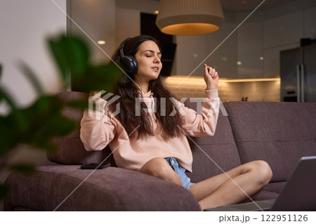 happy Caucasian woman listening to music with headphones on couch at home happy Caucasian woman listening to music with headphones on couch at home 122951126