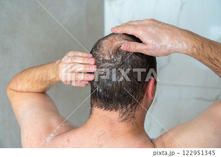 man soaps his head in the shower, head with a bald spot, standing with his back to the camera, close-up shot. High quality 4k footage man soaps his head in the shower, head with a bald spot, standing with his back to the camera, close-up shot. High quality 4k footage 122951345