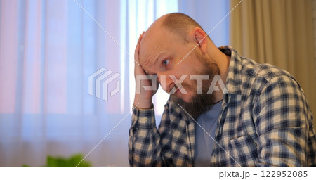 Bald man rubs forehead while stress builds in hectic workspace letting stress overshadow tasks if stress remains unchecked, warning viewers of potential burnout hazards. Remote work of man at computer 122952085