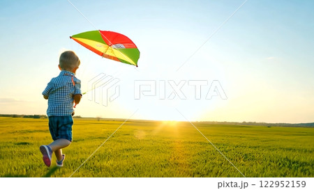 Young boy flying colorful kite, running through grassy meadow at golden sunset, embodying pure childhood joy and freedom. Childhood concept, carefree childhood with a kite in a field. 122952159