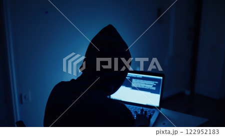Hacker hacks programs. Computer scammer. Programmers working intently on laptop, typing in dark room with shadowy atmosphere, evoking cybersecurity intensity and digital intrigue Hacker hacks programs. Computer scammer. Programmers working intently on laptop, typing in dark room with shadowy atmosphere, evoking cybersecurity intensity and digital intrigue 122952183