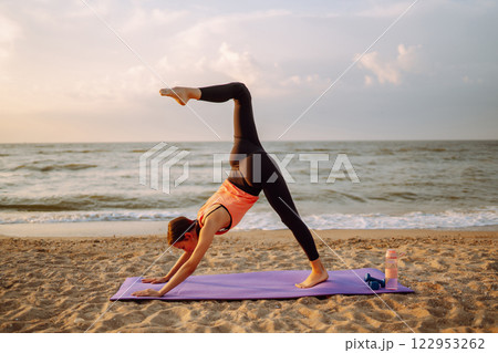Modern young woman doing yoga on beach at sunrise. Concept of an active lifestyle, yoga or fitness. 122953262