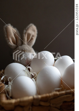 Little bunny peeking behind a basket with eggs . Dark background 122953594