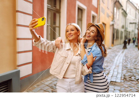 Happy female tourists in casual clothes walk along streets of Europe, take selfies. Active lifestyle 122954714
