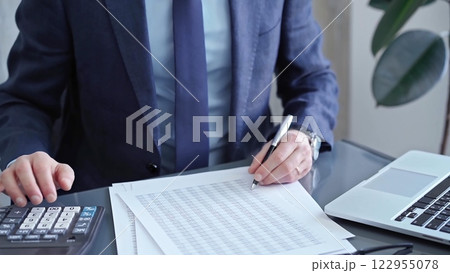 Businessman analyzing financial data on laptop and calculator. Close-up of a professional auditor working on financial reports. Business concept Businessman analyzing financial data on laptop and calculator. Close-up of a professional auditor working on financial reports. Business concept 122955078
