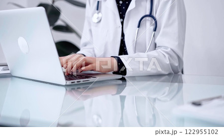 Doctor woman is typing on laptop computer at glass table in clinic, horizontal view. Medicine and pharmacy concept 122955102