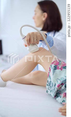 Doctor and kid patient. Orthopedist performing ultrasound examination on a child's knee in a clinic. Medicine and health care 122955139