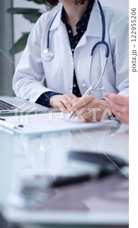 Doctor and patient. Female physician is sitting at the glass table, listening a senior man and writing medication history records. Medicine concept 122955206