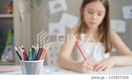 A close-up of colored pencils on the desk, with a creative young girl drawing in the background A close-up of colored pencils on the desk, with a creative young girl drawing in the background 122955208