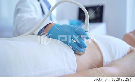 Doctor man wearing a blue medical gloves using an ultrasound equipment on a female patient lying down in clinic cabinet, close up view. Medicine concept 122955284