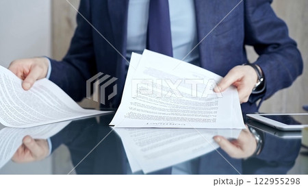 Businessman reviewing documents at office desk. Close-up of a professional man's hands examining paperwork with pen and tablet in sight. Business people concept 122955298