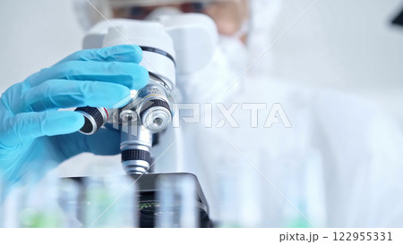 Professional scientist in protective gear is using microscope in a laboratory setting, close-up. Science and medicine concepts 122955331