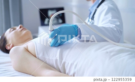 Doctor man, wearing white medical gloves, is using ultrasound equipment on the breast of a female patient. Female breast cancer prevention. Medicine concept Doctor man, wearing white medical gloves, is using ultrasound equipment on the breast of a female patient. Female breast cancer prevention. Medicine concept 122955359