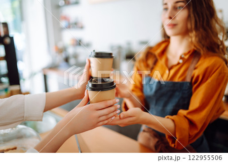 Young woman owner of a coffee shop behind the bar prepares coffee. Concept of orders to go. Young woman owner of a coffee shop behind the bar prepares coffee. Concept of orders to go. 122955506