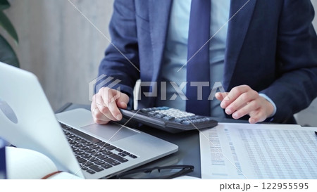 Businessman analyzing financial data on laptop and calculator. Close-up of a professional auditor working on financial reports. Business concept Businessman analyzing financial data on laptop and calculator. Close-up of a professional auditor working on financial reports. Business concept 122955595