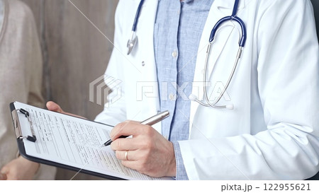Doctor and patient. Close-up of a doctor's hand taking notes on a clipboard with a woman in the background. Medicine and Health care 122955621