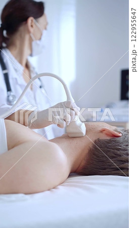 Doctor woman with white medical gloves performing neck ultrasound exam on male patient. Thyroid gland examination. Medicine concept 122955647
