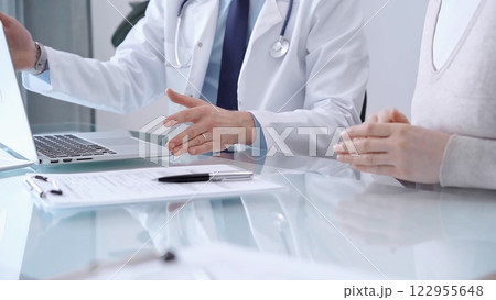 Doctor is consulting patient in modern fair clinic. Healthcare professional discusses medical information with a woman, pointing into the laptop computer monitor. Medicine concept 122955648