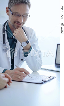 Doctor and a patient. The physician, wearing a white medical coat over a green shirt, gesturing with his hands during a consultation in the clinic. Medicine concept Doctor and a patient. The physician, wearing a white medical coat over a green shirt, gesturing with his hands during a consultation in the clinic. Medicine concept 122955679