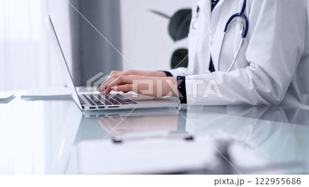 Doctor woman is typing on laptop computer at glass table in clinic, horizontal view. Medicine and pharmacy concept 122955686
