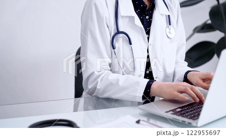 Doctor woman is typing on laptop computer at glass table in clinic. Medicine and pharmacy concept 122955697