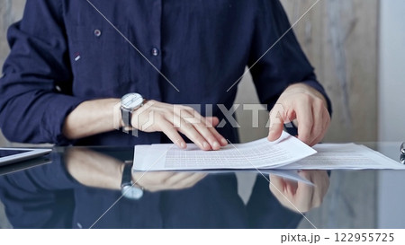 Businessman in dark blue t-shirt analyzing document at desk. Close-up of a professional auditor or lawyer reviewing a lengthy paper report in office setting. Business people concept Businessman in dark blue t-shirt analyzing document at desk. Close-up of a professional auditor or lawyer reviewing a lengthy paper report in office setting. Business people concept 122955725
