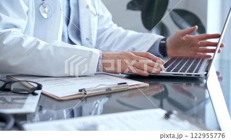 Doctor is using laptop computer in clinic office while sitting at the glass desk. Medicine concept 122955776