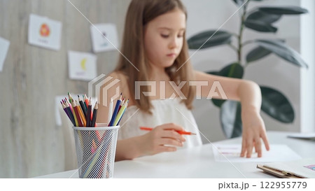 Young girl concentrating on drawing at the desk at home or school class room 122955779