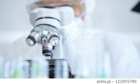 Professional scientist in protective gear is using microscope in a laboratory setting, close-up. Science and medicine concepts 122955780