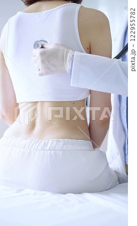 Doctor and patient. Physician wearing white medical gloves is using stethoscope examining woman lungs from the back side in clinic. Medicine and health care 122955782