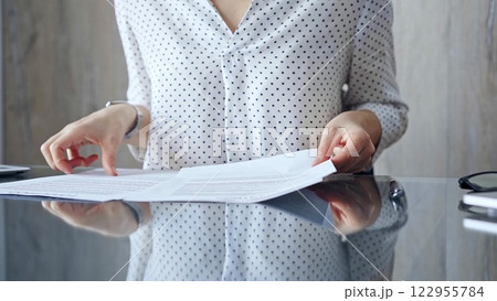 Auditor woman analyzing financial documents with magnifying glass and calculator at her office desk in formal dark blue blouse with polka dots. Business people concept 122955784