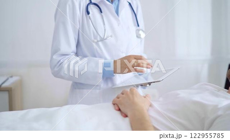 Doctor consulting patient with digital tablet in hospital room. Healthcare professional providing care 122955785