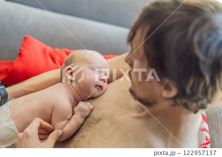 A newborn baby rests peacefully on the father's chest, feeling the warmth and heartbeat of his parent. A tender moment of bonding, love, and security, symbolizing the deep connection between father 122957137