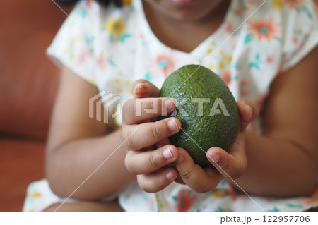 Child holds fresh avocado in hands while sitting indoors 122957706