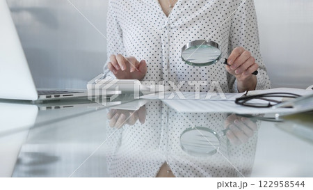Businesswoman carefully reviewing financial reports with magnifying glass and calculator, conducting audit and analyzing data. Taxes, audit in business 122958544